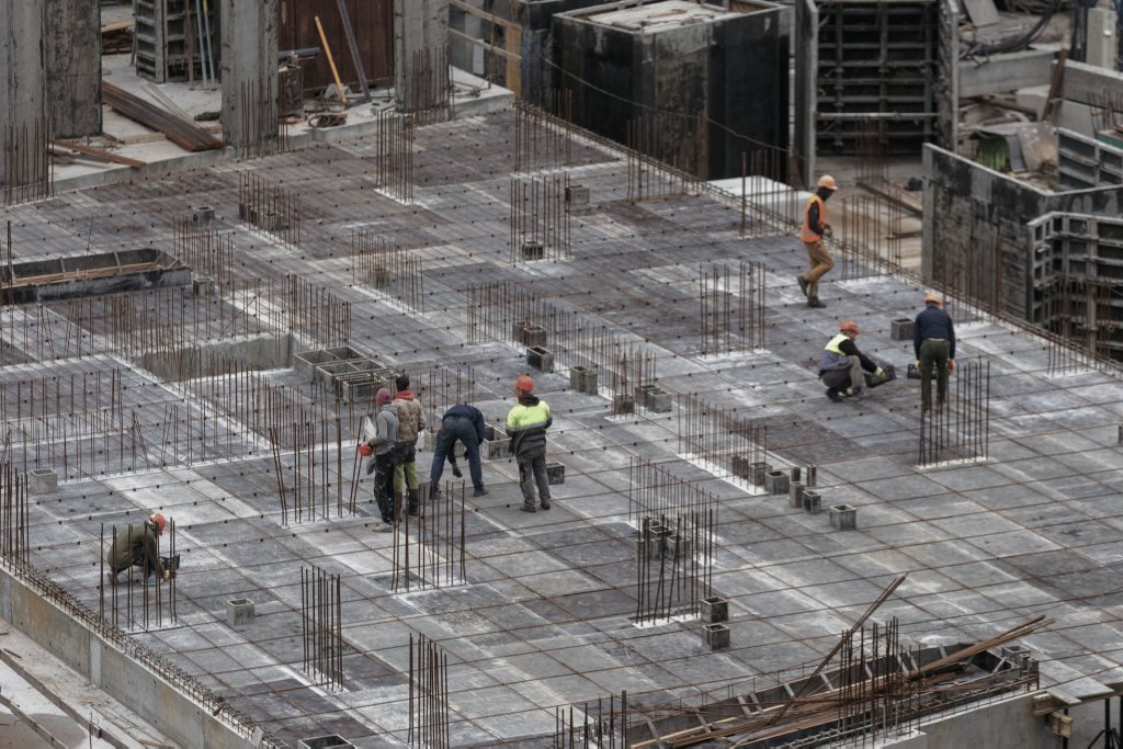 Equipe de operários trabalhando sobre a armação de aço de uma laje de concreto em canteiro de obras