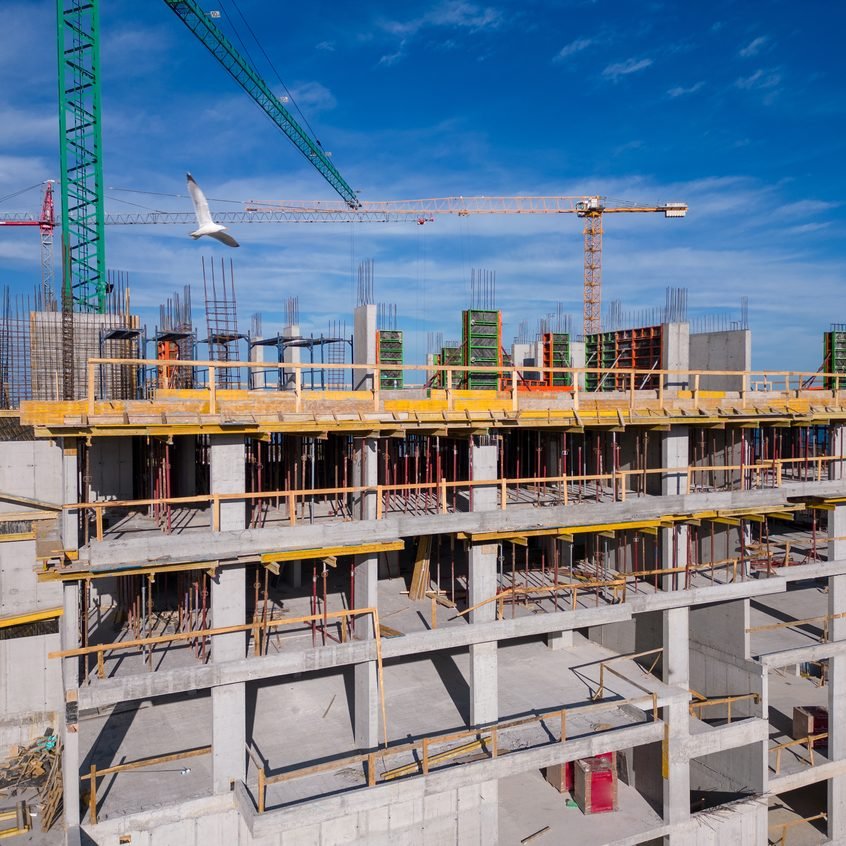 Estrutura de concreto armado de um edifício em construção com gruas ao fundo